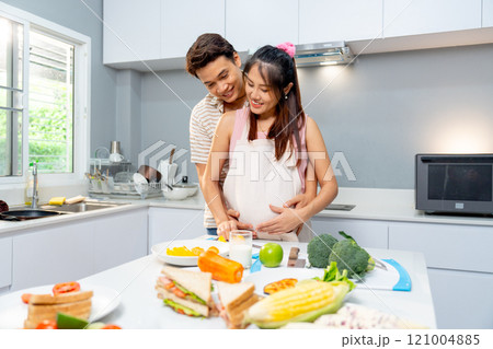 Asian man stand and hug from the back of pregnant woman and during woman prepare to cook in the kitchen of their house. 121004885