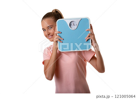 Young attractive smiling girl holding weighing scale and looking to camera, isolated over white background 121005064