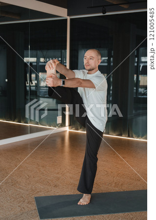 An athletic young man does exercises in the fitness room. A professional guy does yoga in the gym An athletic young man does exercises in the fitness room. A professional guy does yoga in the gym 121005485