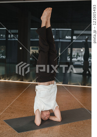 An athletic young man does exercises in the fitness room. A professional guy does yoga in the gym 121005493
