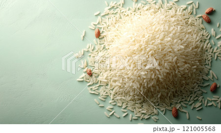 pile of white rice grains scattered on light green surface, surrounded by almonds, creating fresh and natural look 121005568