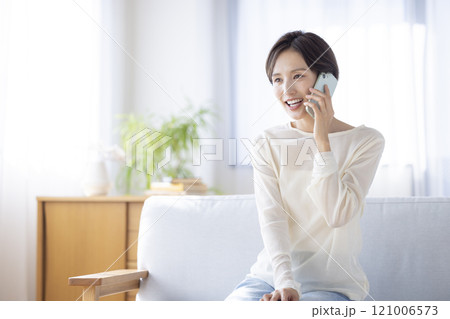 ライフスタイル　ソファーに座りスマホで通話する女性 121006573