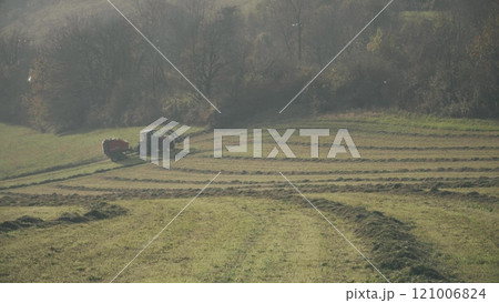 A tractor with hay baler or hay maker trailer in the green field A tractor with hay baler or hay maker trailer in the green field 121006824