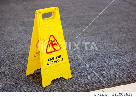 A bright yellow sign displays a caution notice about a wet floor A bright yellow sign displays a caution notice about a wet floor 121009615