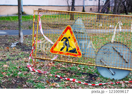 A construction sign in yellow and red color is perched on top of a fence A construction sign in yellow and red color is perched on top of a fence 121009617