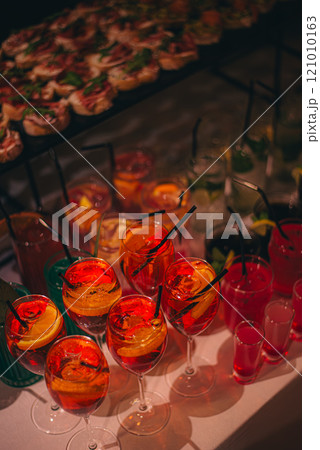 Chilled alcoholic cocktails served on the rocks with rosemary garnish displayed in rows on a buffet table in elegant glasses at a catered event 121010163