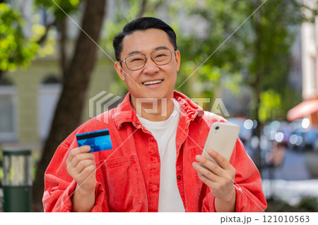 Asian man using credit bank card smartphone while transferring money, purchases online shopping Asian man using credit bank card smartphone while transferring money, purchases online shopping 121010563