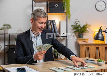 Happy young Caucasian successful businessman in formal suit counting money cash at home office desk Happy young Caucasian successful businessman in formal suit counting money cash at home office desk 121010673