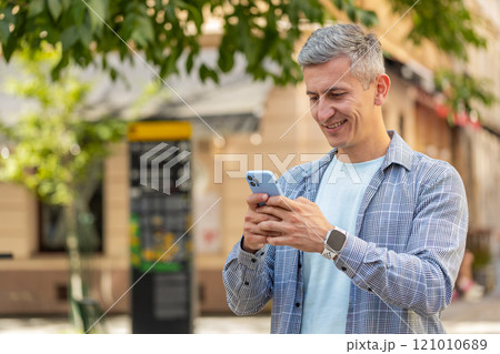 Happy Caucasian man using smartphone typing text messages browsing internet standing on city street 121010689