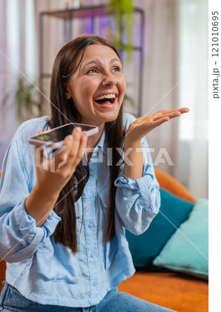 Smiling young Caucasian woman making phone conversation talk with friends sitting on couch at home 121010695