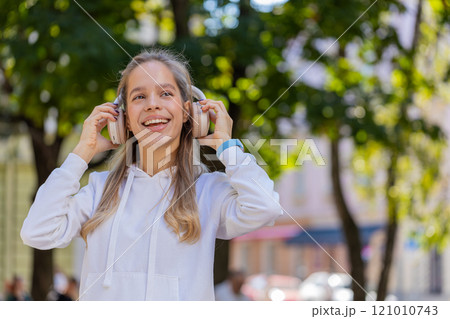 Happy young woman taking off headphones after listening favorite energetic music on city street 121010743