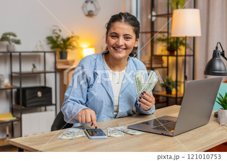Happy rich Indian freelancer counting money cash using smartphone calculator app at home office desk 121010753