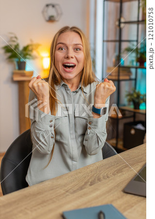 Happy Caucasian woman looking at camera shocked by sudden victory sitting at home office table 121010758
