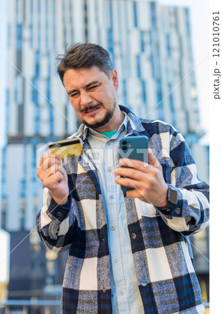 Frustrated mature businessman using credit card and mobile phone standing on downtown city street 121010761