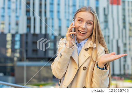 Mature Caucasian businesswoman having remote conversation on smartphone on downtown city street 121010766