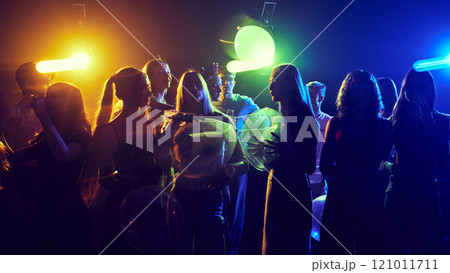Young cheerful girls and boys, friends attending party, celebrating birthday or holiday together,. cheerfully dancing under neon lights 121011711