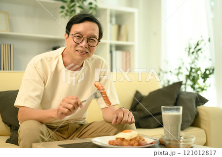 Happy middle aged man sitting on sofa, enjoying a plate of fried rice Happy middle aged man sitting on sofa, enjoying a plate of fried rice 121012817