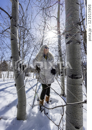 Smiling woman snowshoeing through aspen forest 121013908