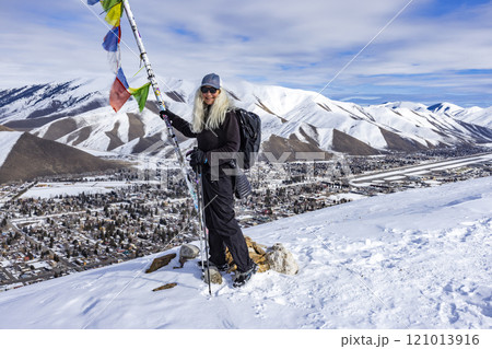 Smiling woman with snowshoes standing at pole with colorful flags on top of mountain 121013916
