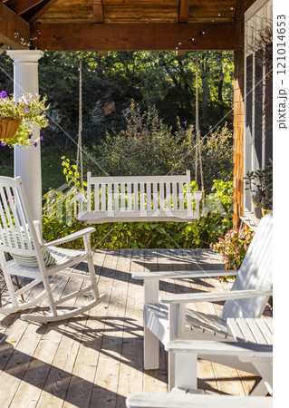 Rocking chair and swing on front porch of cottage house 121014653