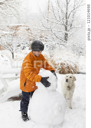 Boy with his dog building snowman 121014698