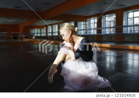 Pensive ballerina sitting on floor in ballet studio Pensive ballerina sitting on floor in ballet studio 121014916