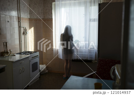 Rear view of woman looking through window in kitchen 121014937