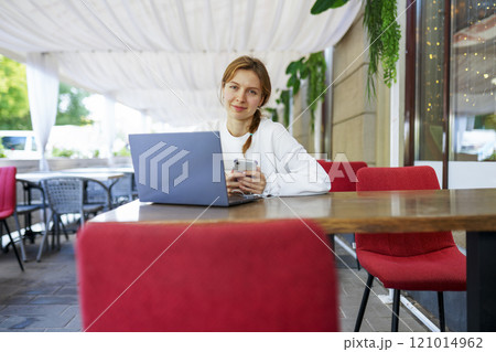 Portrait of smiling woman with smart phone and laptop at cafe table Portrait of smiling woman with smart phone and laptop at cafe table 121014962
