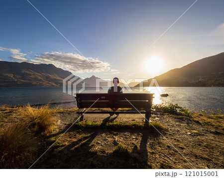 Rear view of woman sitting on bench, facing Lake Wakatipu at sunset 121015001