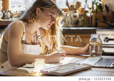 Teenage girl painting with watercolors at table 121015198