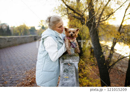 Woman with Yorkshire Terrier by river in autumn Woman with Yorkshire Terrier by river in autumn 121015209