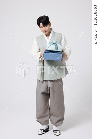 Portrait of a young man wearing hanbok and holding a luxurious holiday gift 121016063