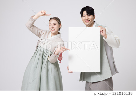A foreign woman and a Korean man wearing hanbok, standing side by side and holding white copyspace A foreign woman and a Korean man wearing hanbok, standing side by side and holding white copyspace 121016139