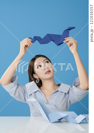 Portrait of a woman sitting and posing while holding a blue snake folded out of paper 121016357