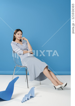 A woman sitting and posing in front of a blue snake folded out of paper 121016383