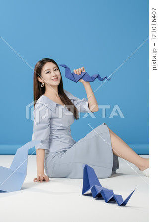 A woman sitting and posing in front of a blue snake folded out of paper A woman sitting and posing in front of a blue snake folded out of paper 121016407