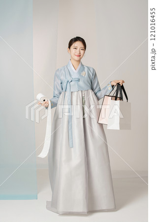 A beautiful woman standing wearing an elegant and elegant hanbok, holding a shopping bag and a receipt stretched out like a roll of toilet paper. 121016455