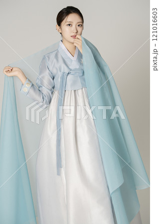 A beautiful woman wearing a luxurious and elegant Hanbok, standing draped in blue cloth. 121016603