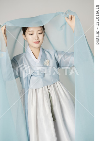 A beautiful woman wearing a luxurious and elegant Hanbok, standing draped in blue cloth. 121016618