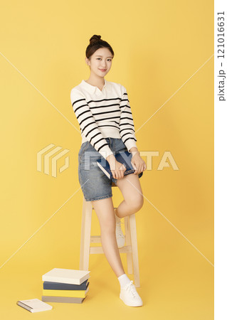Portrait of a college student wearing casual clothes posing while sitting on a chair holding a book Portrait of a college student wearing casual clothes posing while sitting on a chair holding a book 121016631
