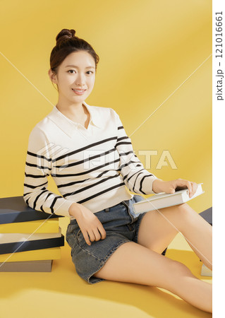 A college student wearing casual clothes and sitting on the floor reading 121016661