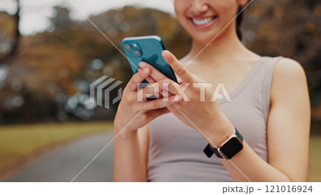 Smile, woman and hands with phone for fitness outdoor, communication and research of exercise application. Happy, athlete and mobile for gym membership, training schedule and workout routine in Japan 121016924