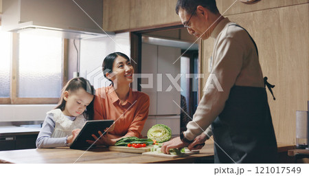 Mom, girl and tablet in kitchen with dad, cooking and happy with streaming, recipe and teaching in family home. People, mother and daughter with touchscreen, food and meal prep at house in Japan 121017549