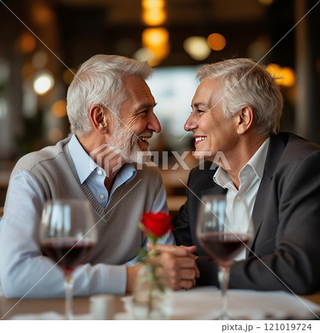 An elderly couple sharing laughter and love during a romantic dinner at a cozy restaurant, with wine and a rose on the table 121019724