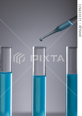 Vertical image of laboratory test tubes with blue liquid, pipette and copy space on grey background 121019921