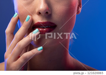 Caucasian woman wearing red lipstick and blue nail polish on blue background Caucasian woman wearing red lipstick and blue nail polish on blue background 121020065