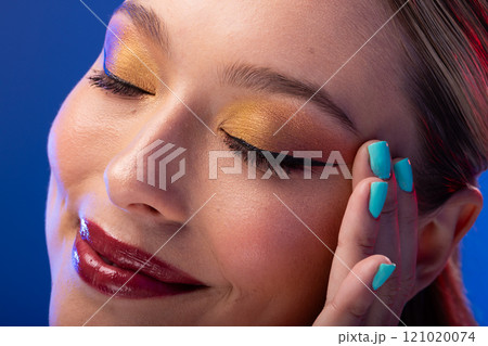 Caucasian woman with brown hair wearing golden eye shadow and blue nail polish on blue background Caucasian woman with brown hair wearing golden eye shadow and blue nail polish on blue background 121020074