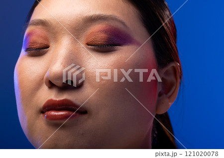 Asian woman with black hair wearing purple eye shadow and red lipstick on blue background 121020078