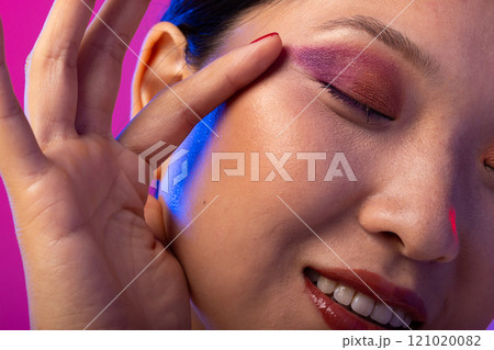 Asian woman with black hair wearing purple eye shadow and red nail polish on purple background 121020082