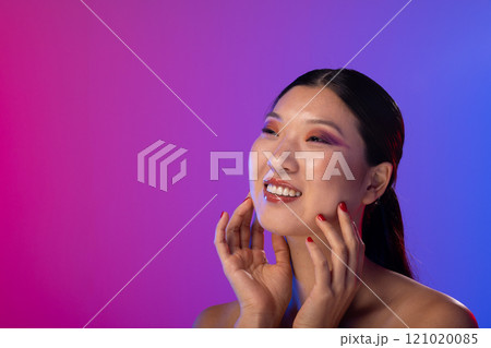 Asian woman wearing purple eye shadow and red nail polish on purple background, copy space 121020085